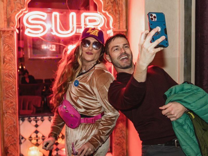 Brianna and a guest taking a selfie under the SUR neon sign