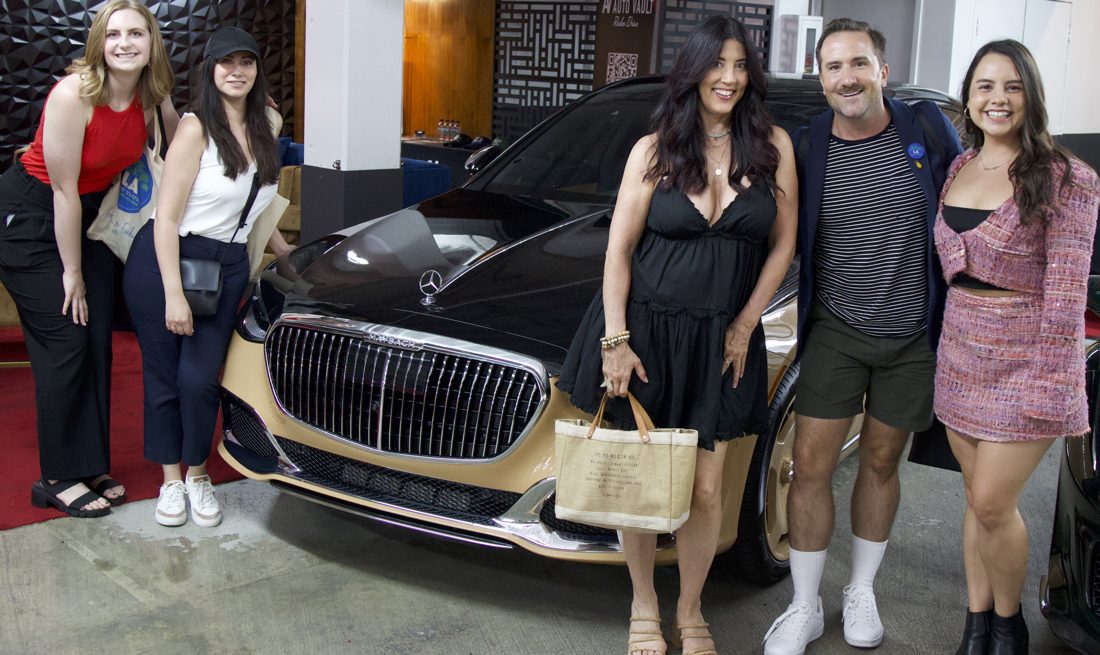 Guests posing beside a luxury car in a Beverly Hills showroom